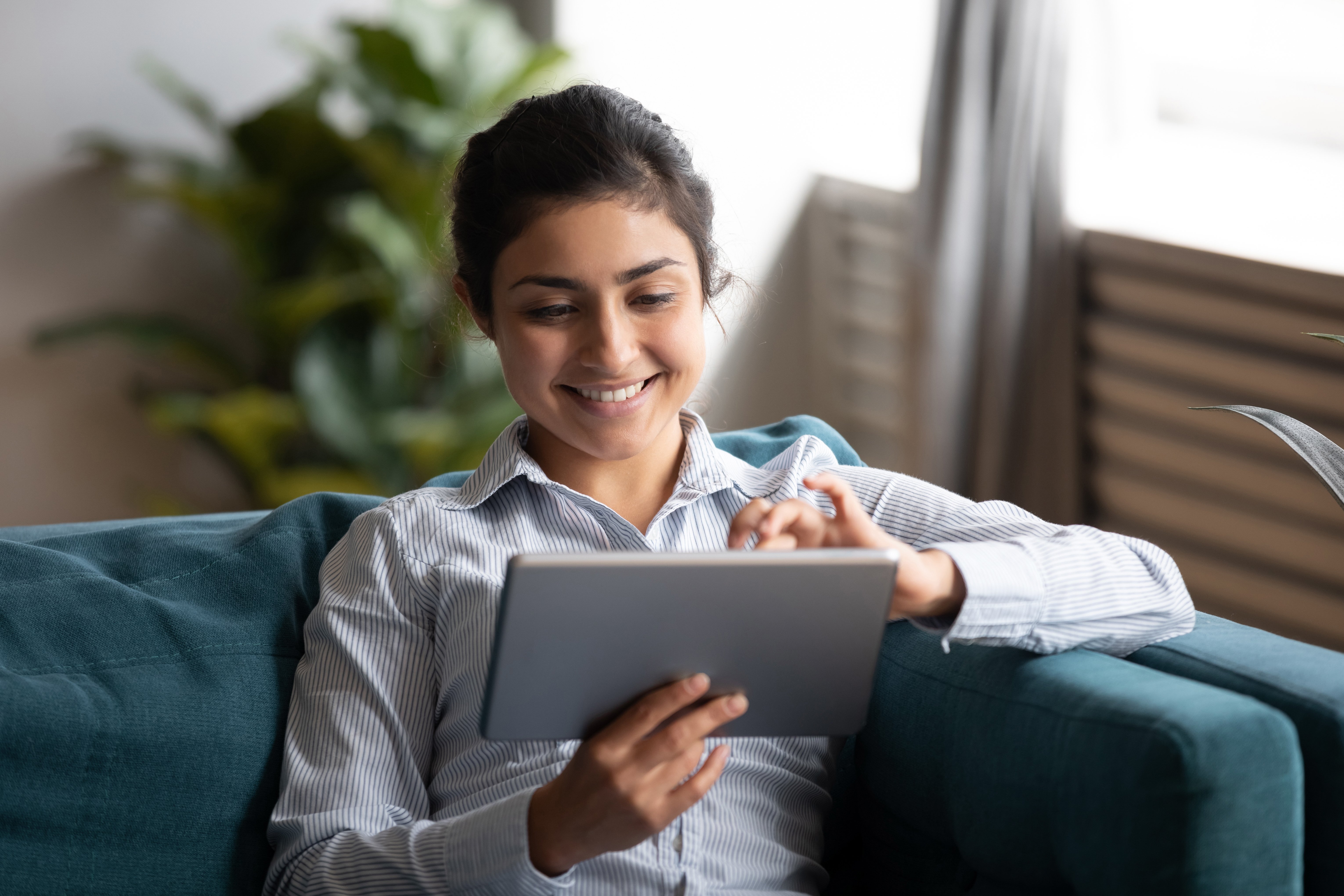 Happy-indian-woman-using-tablet-sit-on-sofa-at-home-1198252613_6121x4081