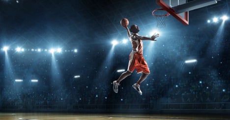 Male basketball player jumps to make a slam dunk during a March Madness game.