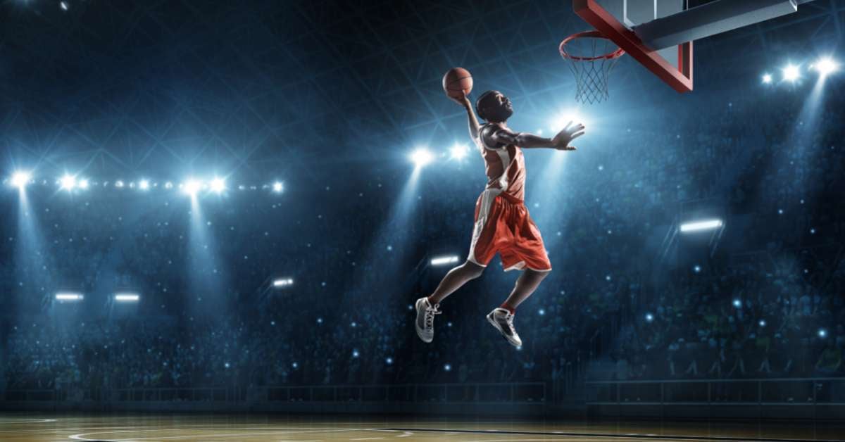 Male basketball player jumps to make a slam dunk during a March Madness game.