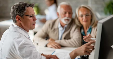 An insurance agent points to a screen monitor to go over insurance risks with an elderly couple. 