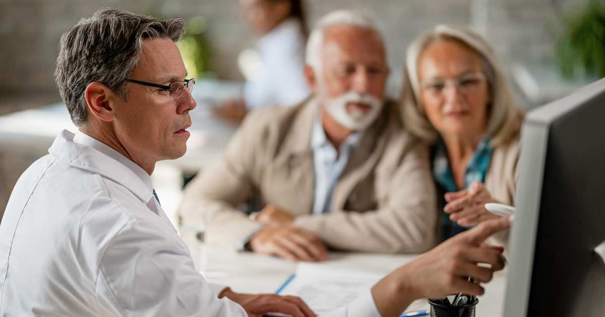An insurance agent points to a screen monitor to go over insurance risks with an elderly couple. 