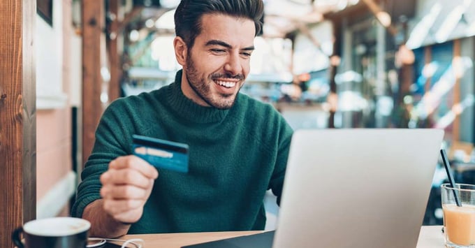 Man smiles and holds a credit card to make an online purchase.
