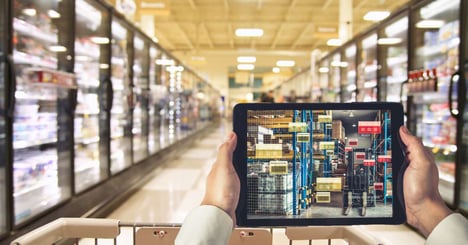 Image of a person holding a tablet with a online grocery management system while standing in a grocery aisle.