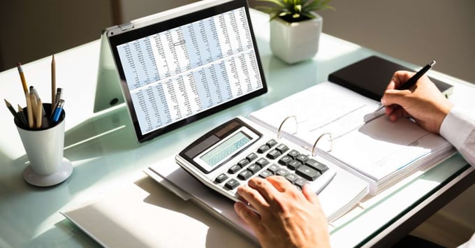 An image of a person's hand calculating billing with a tablet and calculator. 
