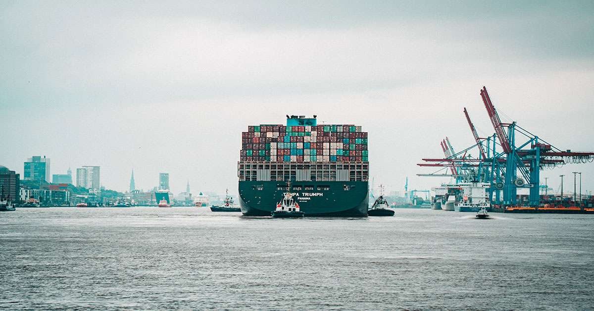 A cargo ship hauls off a load of supplies guided by a tug boat.