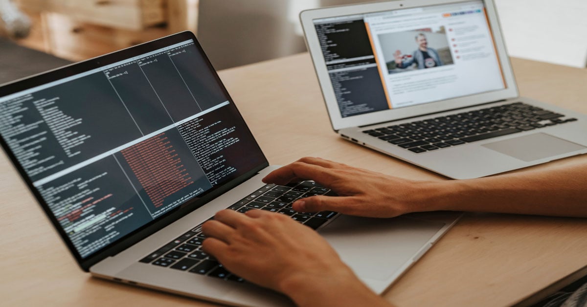  A man is performing web services testing by typing testing code into one silver laptop while running the test code on the website of another silver laptop.