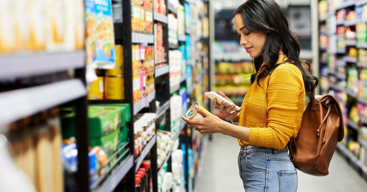 Woman stands in the grocery aisle scanning the price of a product using the grocery store's system