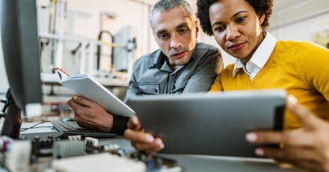 A man and woman sit at a desk and look over automation testing on a tablet.