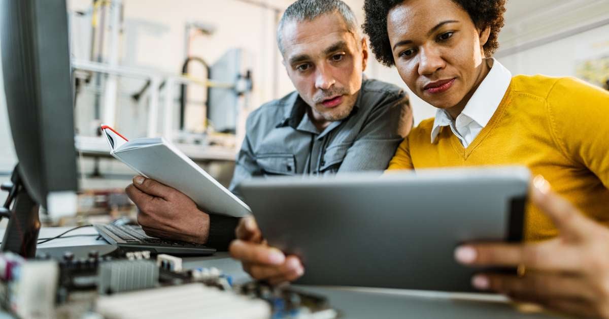 A man and woman sit at a desk and look over automation testing on a tablet.